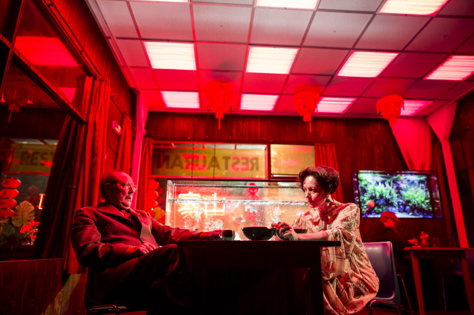 Scene from Łukasz Twarkowski’s ROTHKO at the Holland Festival featuring a mirrored Chinese restaurant set with actors performing live while a stylized close-up video feed is projected on a massive LED screen above the stage.