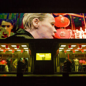 Scene from Łukasz Twarkowski’s ROTHKO at the Holland Festival featuring a mirrored Chinese restaurant set with actors performing live while a stylized close-up video feed is projected on a massive LED screen above the stage.